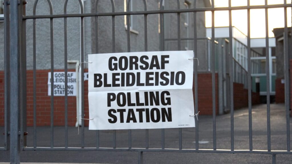 Poster which reads 'Gorsaf Bleidleisio, Polling Station' attached to gate 