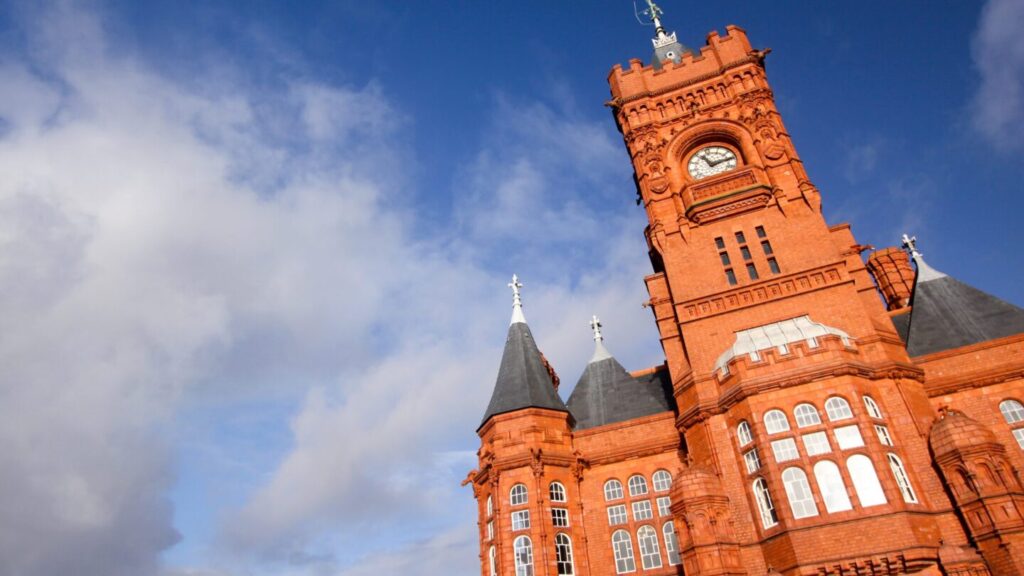 Outside of the Pierhead building. It is tall with vibrant red bricks and a clock on what looks like a tower. 