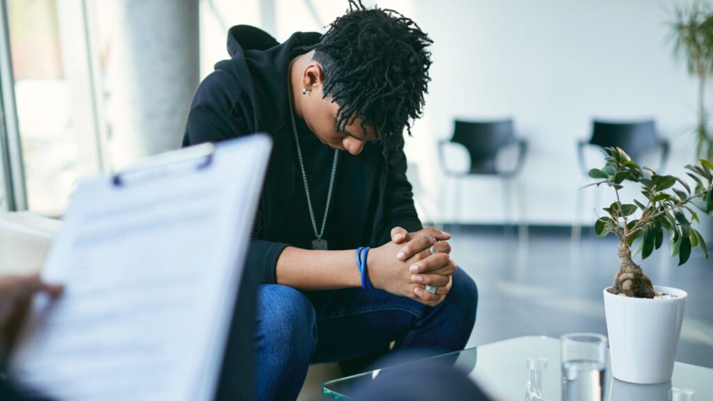 Teen boy sat in counsellors office, looking down and ashamed