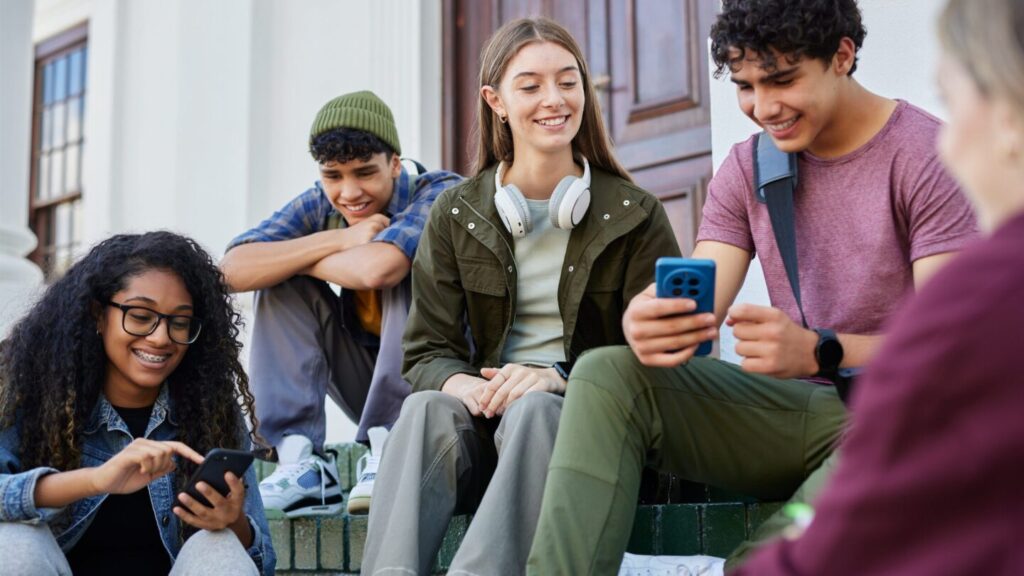 Group of teens sat on steps outside using their mobile phones