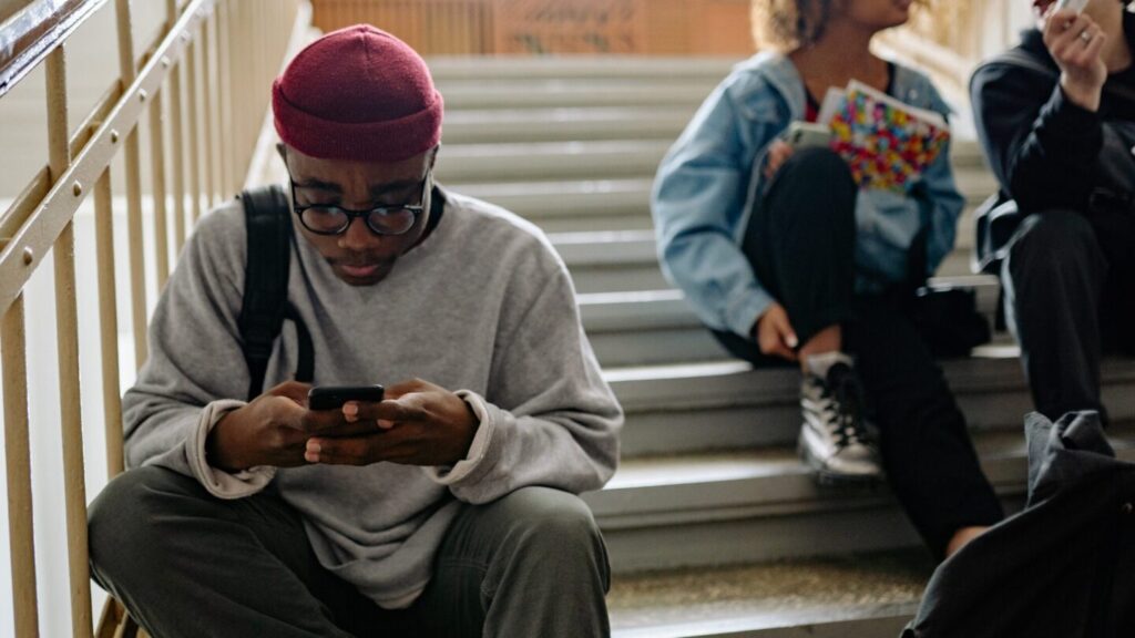 Teen boy sat on steps looking down at his phone, concentrating