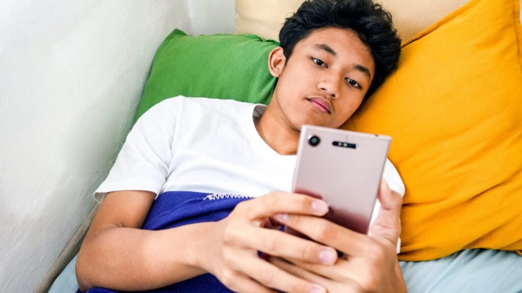 Teen boy in bed using his mobile phone