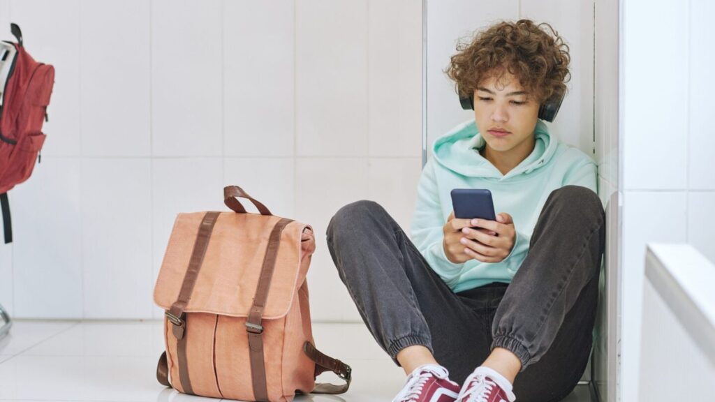 Teen boy sat on the floor in his bedroom looking at his phone